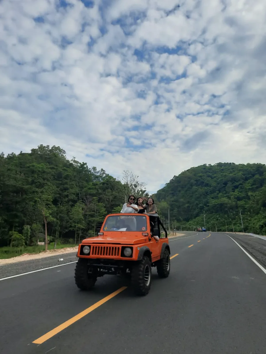 Pengunjung berdiri di atas jip oranye dalam perjalanan Trip Dewi Kampus